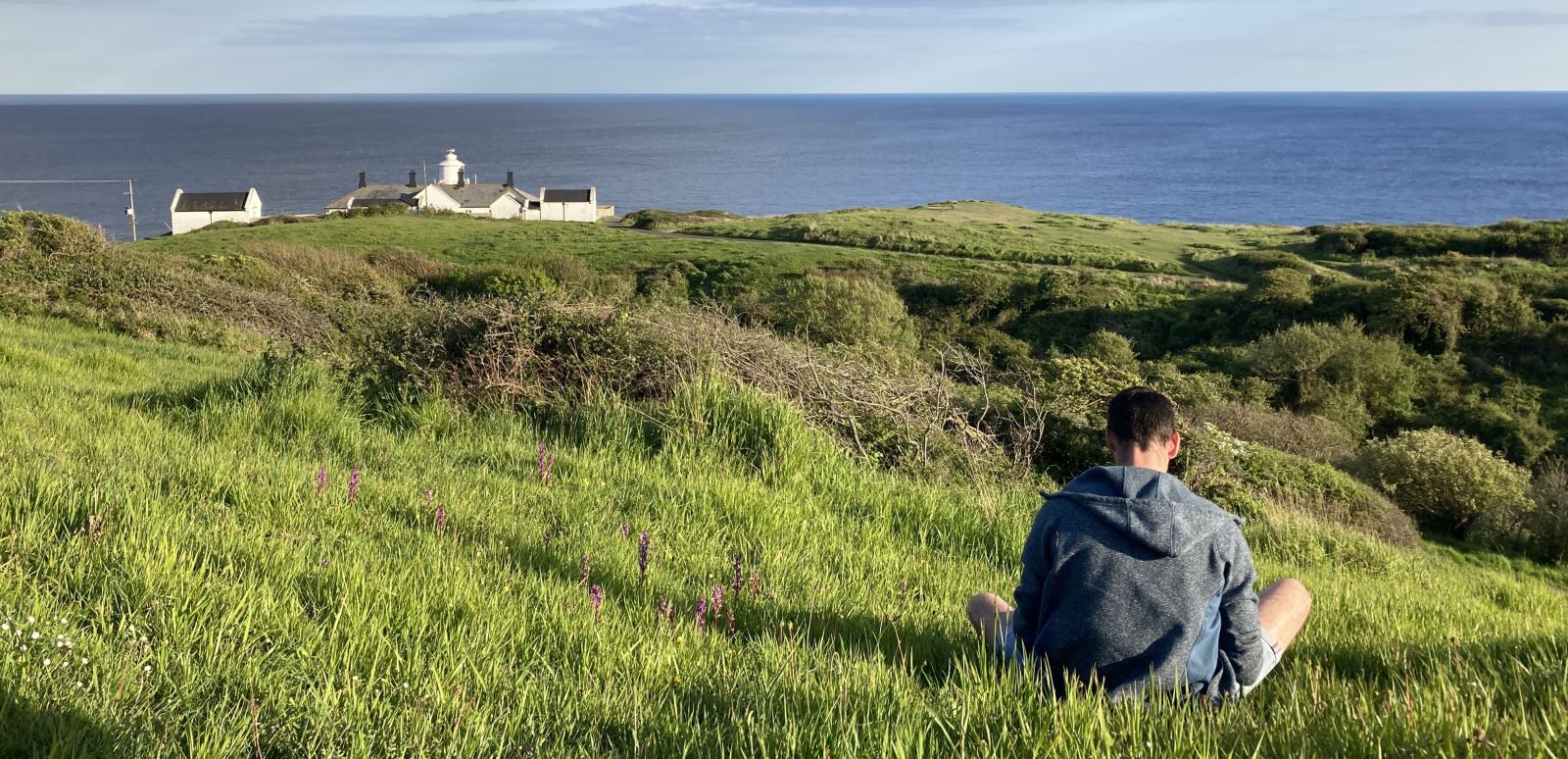 Man sat in grass overlooking Lighthouse and sea